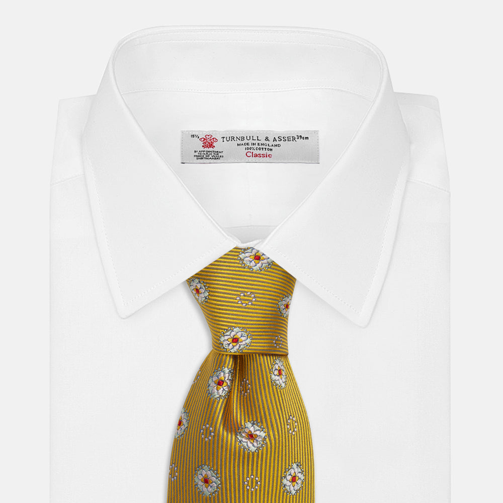 The Yellow Multi Floral Motif Silk Tie by Turnbull & Asser features subtle diagonal stripes and small white, blue, and orange floral motifs—a perfect summer palette, shown rolled up on a plain white background.