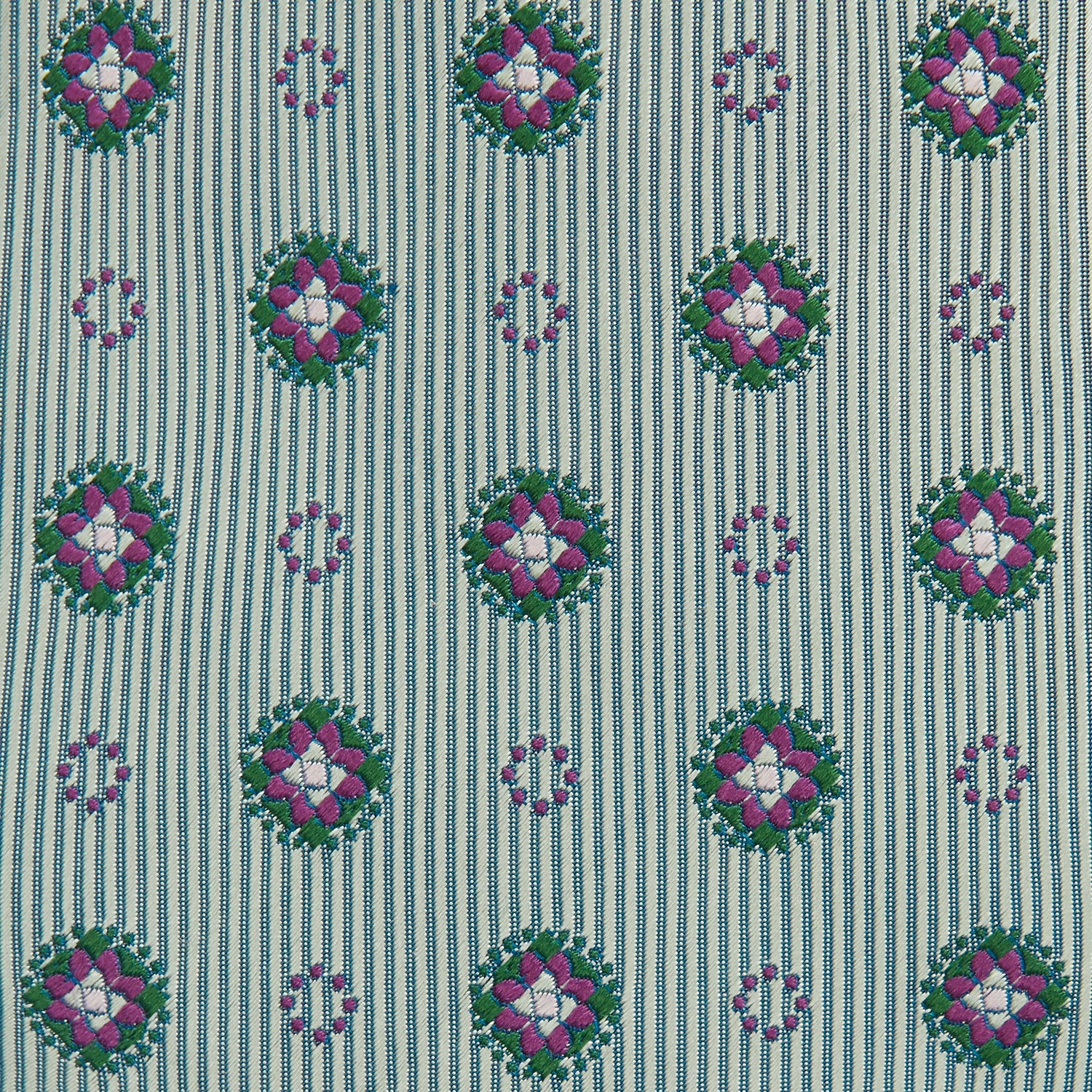 View 3 of product The Green Multi Floral Motif Silk Tie by Turnbull & Asser features light gray silk with thin diagonal stripes and a floral medallion pattern in pink, purple, and green—ideal for adding summer color to your outfit. Displayed rolled up on a white background.