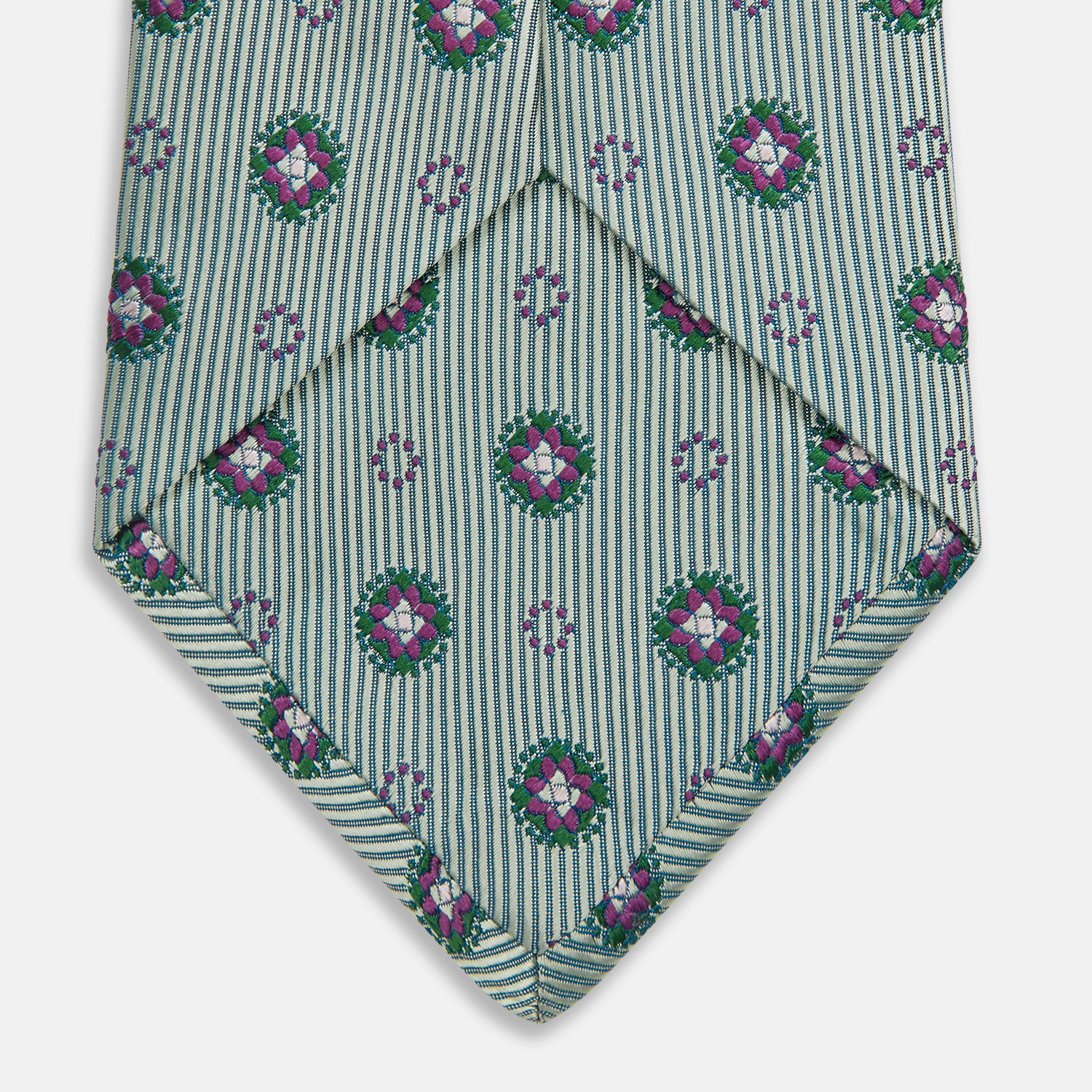 View 4 of product The Green Multi Floral Motif Silk Tie by Turnbull & Asser features light gray silk with thin diagonal stripes and a floral medallion pattern in pink, purple, and green—ideal for adding summer color to your outfit. Displayed rolled up on a white background.