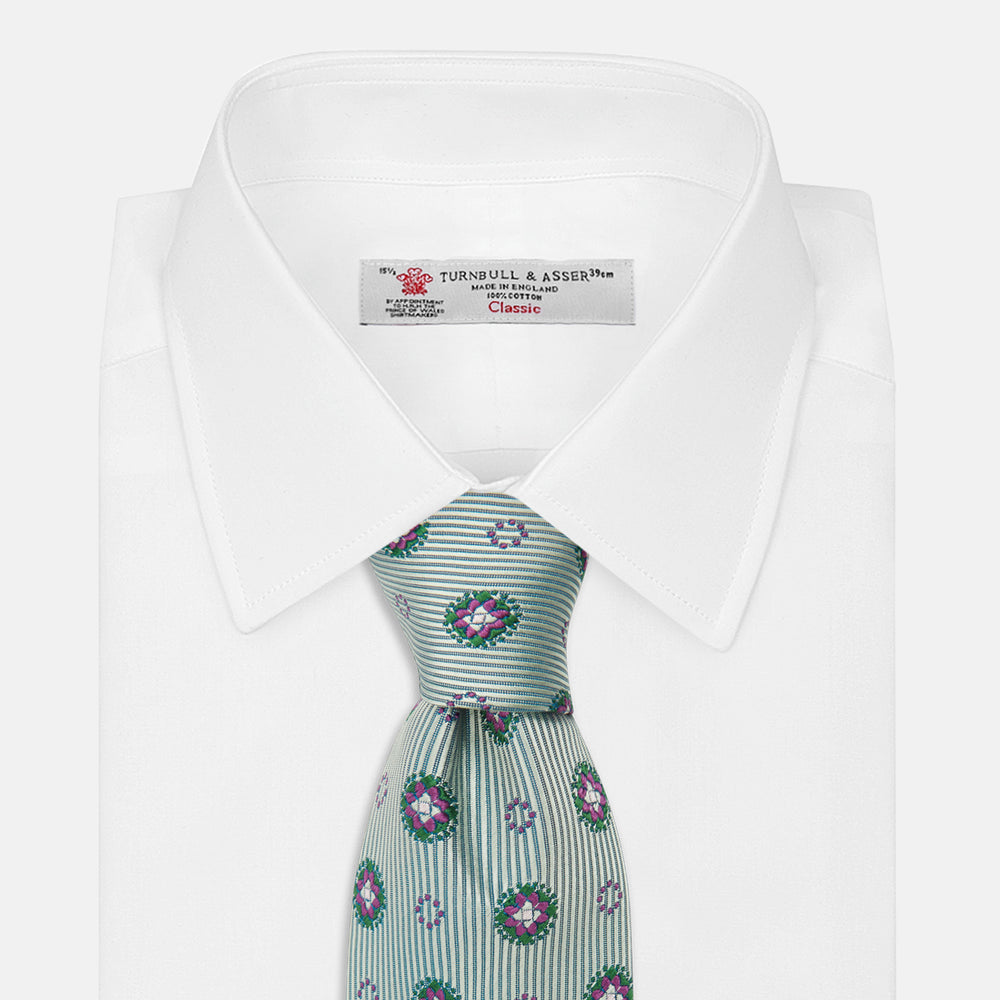 The Green Multi Floral Motif Silk Tie by Turnbull & Asser features light gray silk with thin diagonal stripes and a floral medallion pattern in pink, purple, and green—ideal for adding summer color to your outfit. Displayed rolled up on a white background.