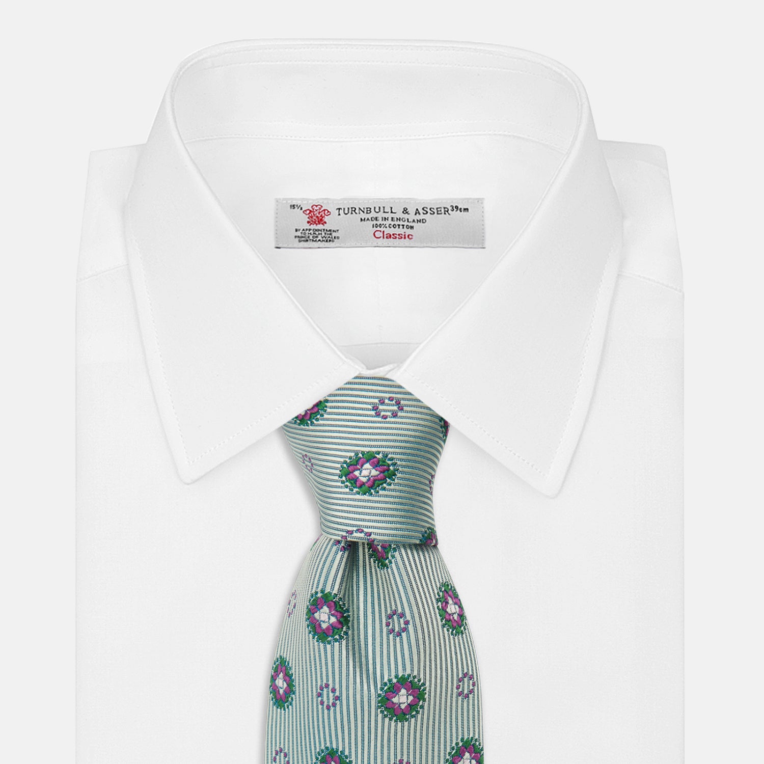 View 2 of product The Green Multi Floral Motif Silk Tie by Turnbull & Asser features light gray silk with thin diagonal stripes and a floral medallion pattern in pink, purple, and green—ideal for adding summer color to your outfit. Displayed rolled up on a white background.