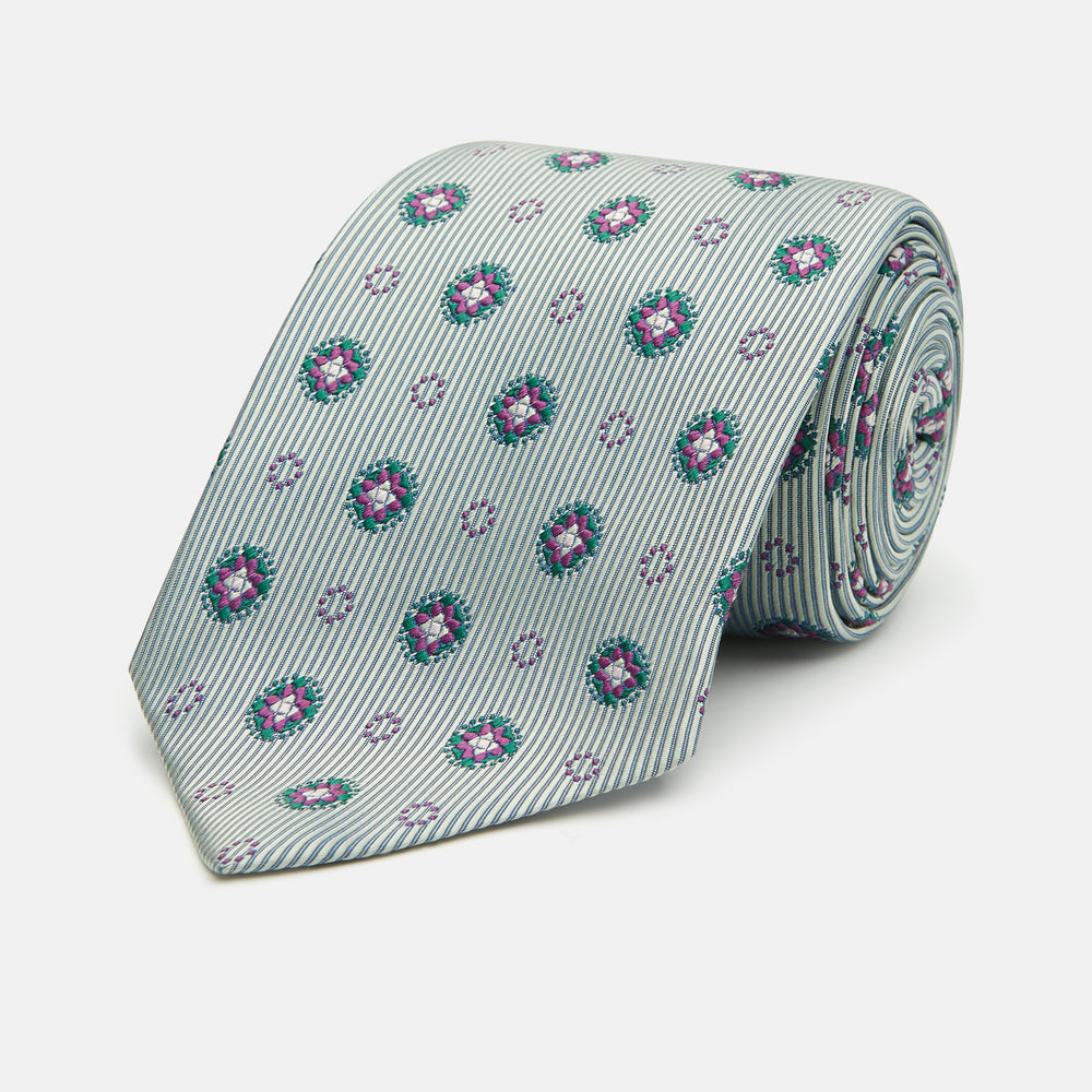 The Green Multi Floral Motif Silk Tie by Turnbull & Asser features light gray silk with thin diagonal stripes and a floral medallion pattern in pink, purple, and green—ideal for adding summer color to your outfit. Displayed rolled up on a white background.