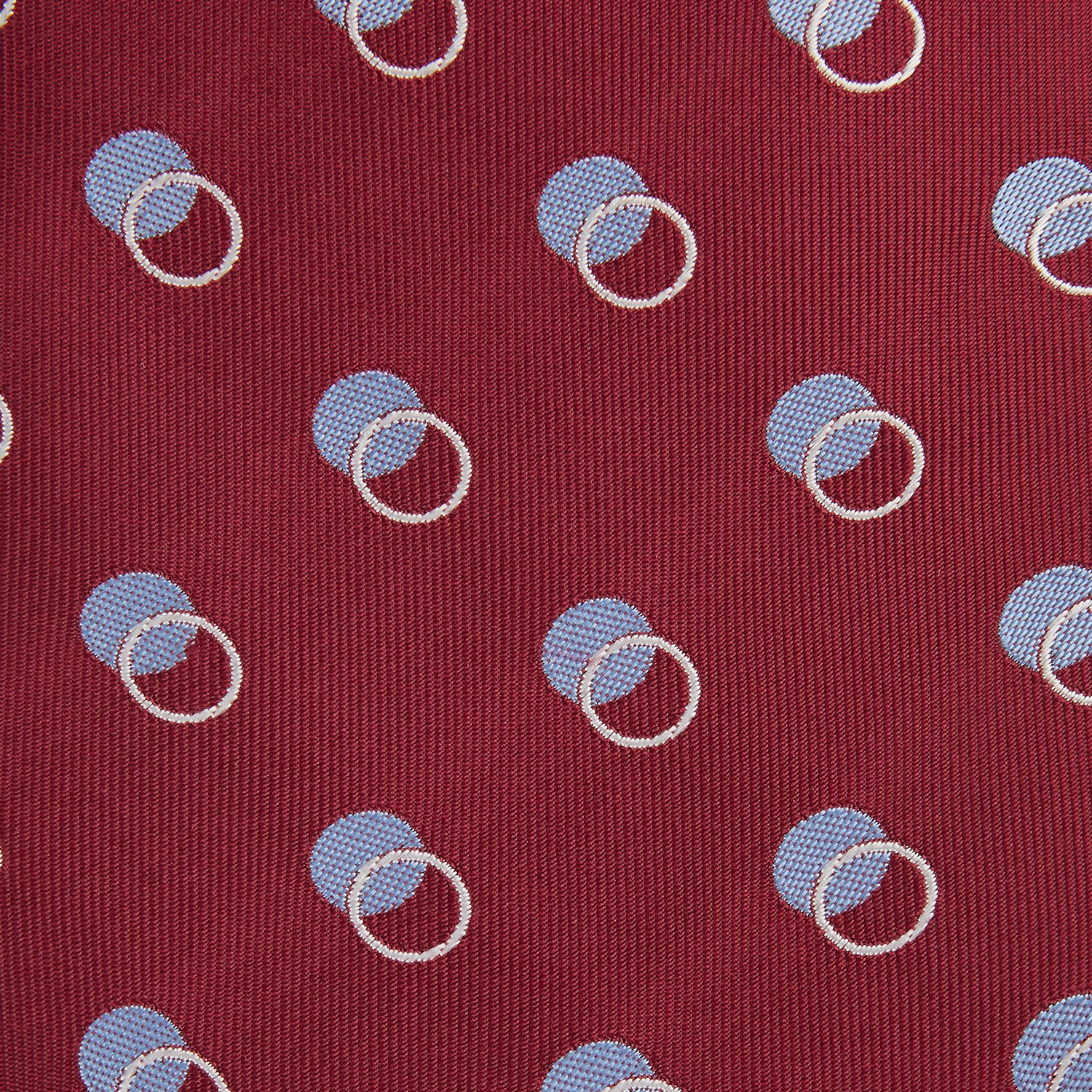 View 3 of product The Turnbull & Asser Red Multi Circle Silk Tie features small blue and white rings on red silk, making it ideal for pairing with bold shirts or adding vibrant flair to summer looks. Shown rolled at one end against a plain white background.