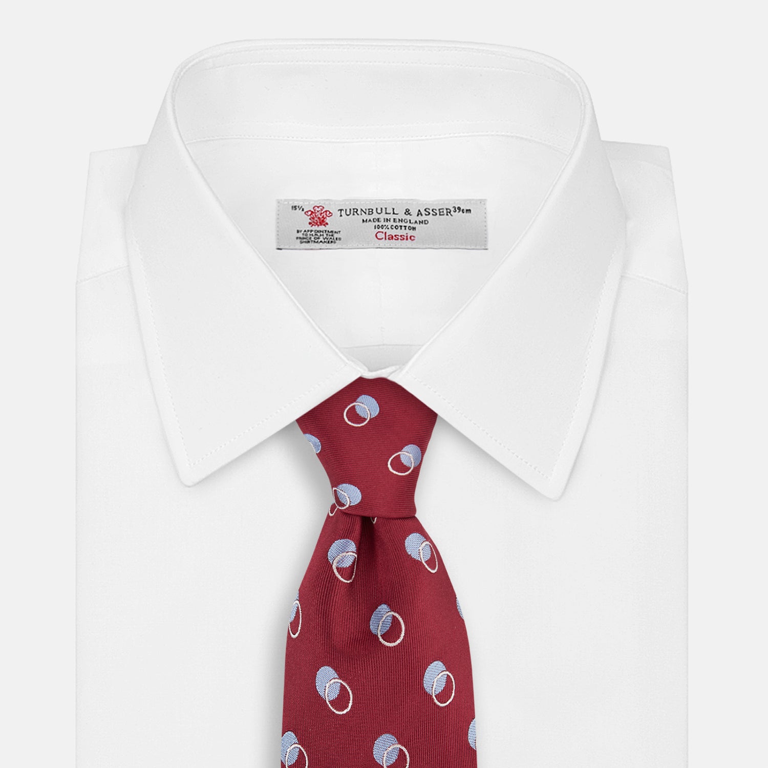 View 2 of product The Turnbull & Asser Red Multi Circle Silk Tie features small blue and white rings on red silk, making it ideal for pairing with bold shirts or adding vibrant flair to summer looks. Shown rolled at one end against a plain white background.