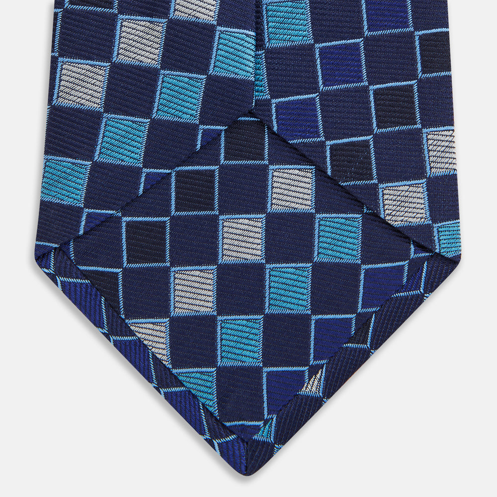 The Blue Multi Check Silk Tie by Turnbull & Asser features a geometric checked pattern in blue, light blue, and silver on dark navy—ideal for pairing with bold shirts.