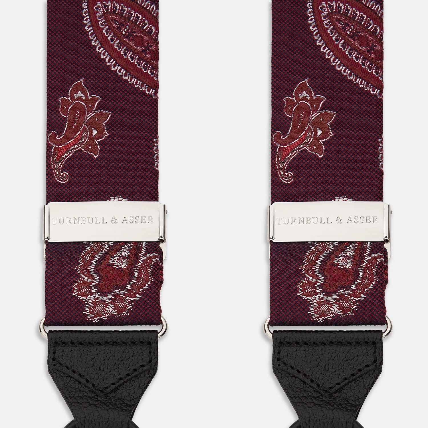 View 2 of product Two red paisley adjustable silk braces by Turnbull & Asser, featuring leather ends and silver clasps, are laid out vertically side by side on a white background.