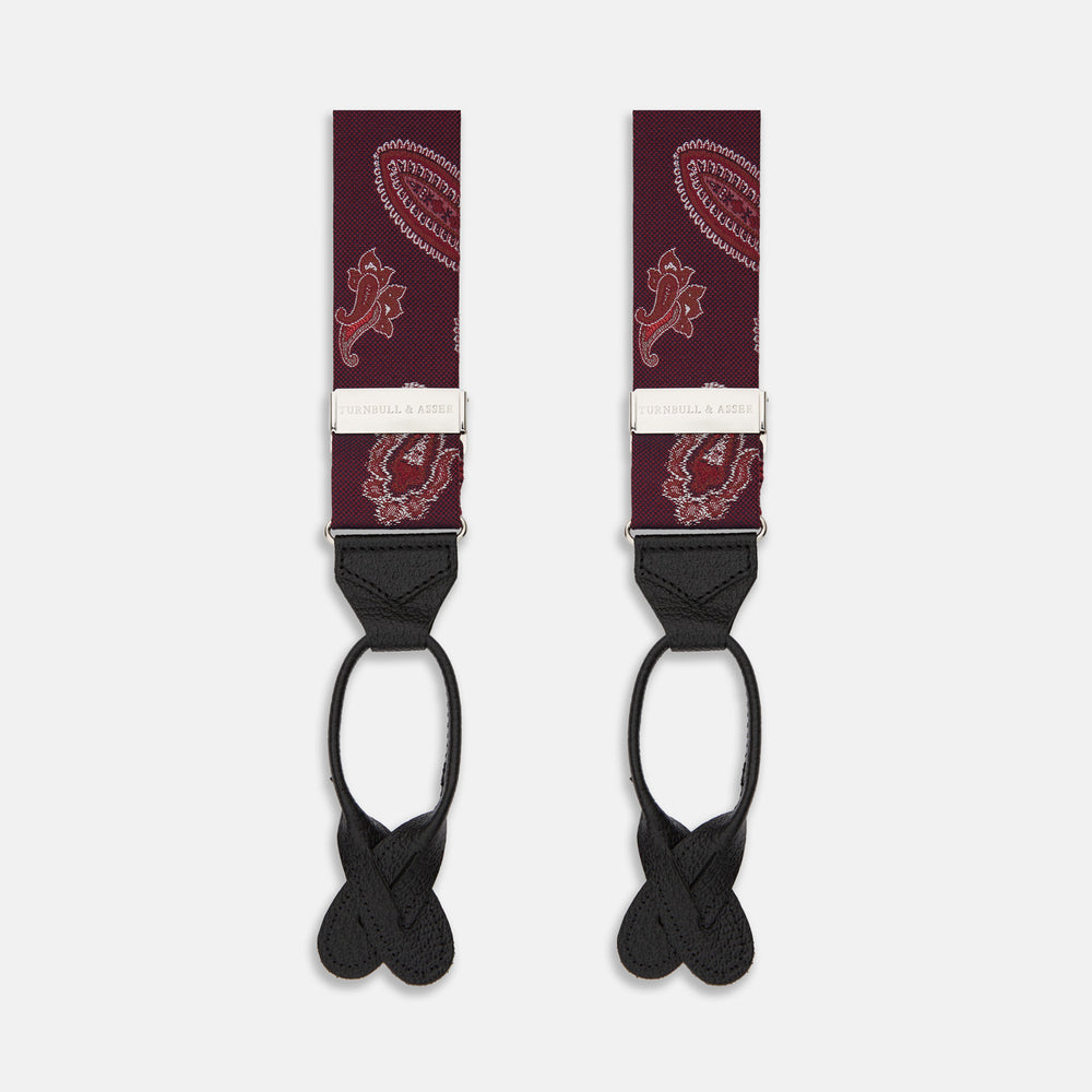 Two red paisley adjustable silk braces by Turnbull & Asser, featuring leather ends and silver clasps, are laid out vertically side by side on a white background.