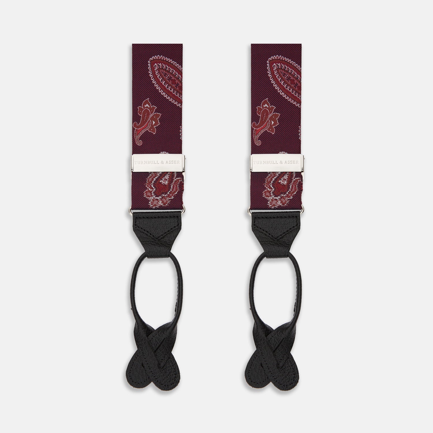View 1 of product Two red paisley adjustable silk braces by Turnbull & Asser, featuring leather ends and silver clasps, are laid out vertically side by side on a white background.