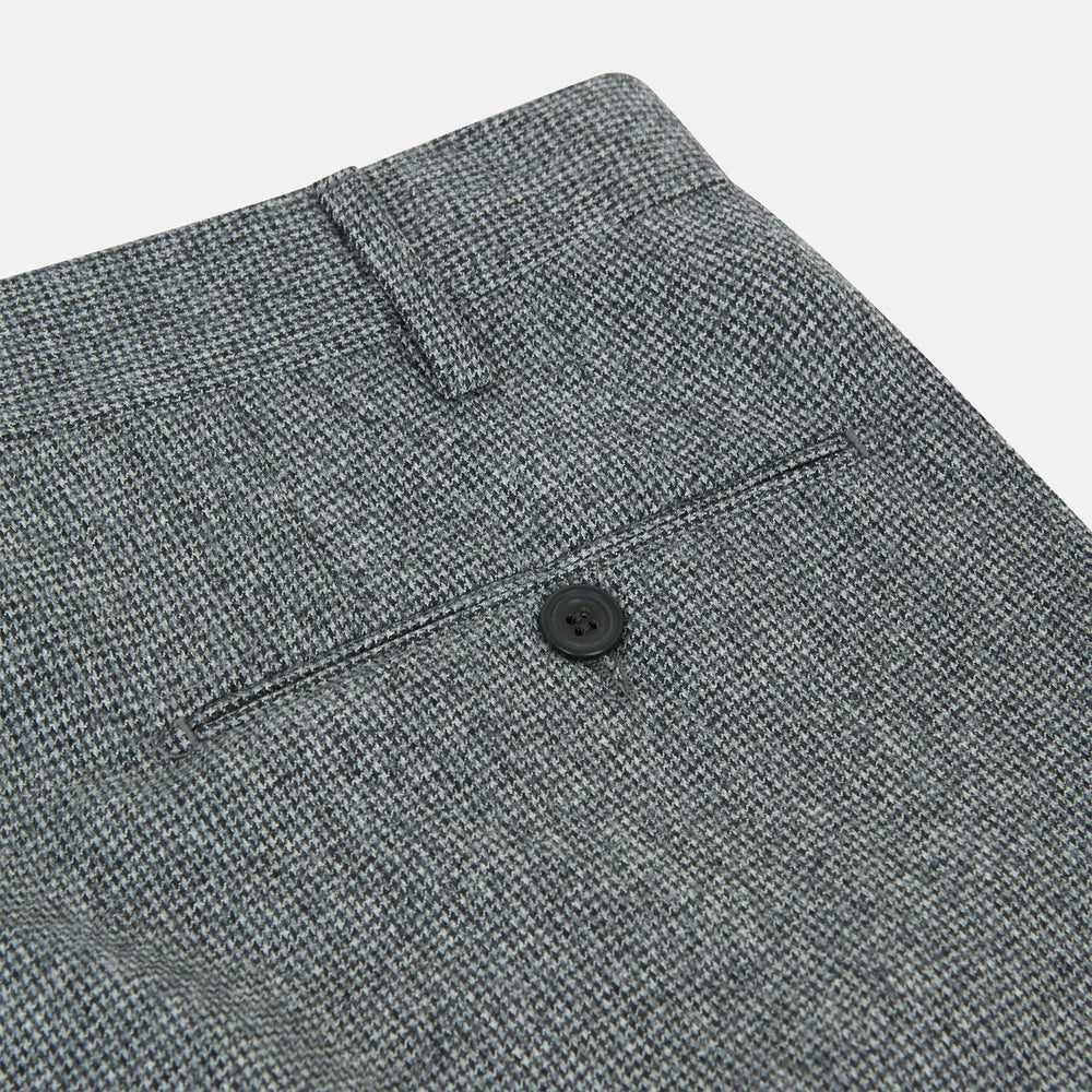 A person wears Turnbull & Asser Grey Puppytooth Wool Manson Trousers, a white dress shirt with rolled-up sleeves, and black shoes, standing against a plain beige background.