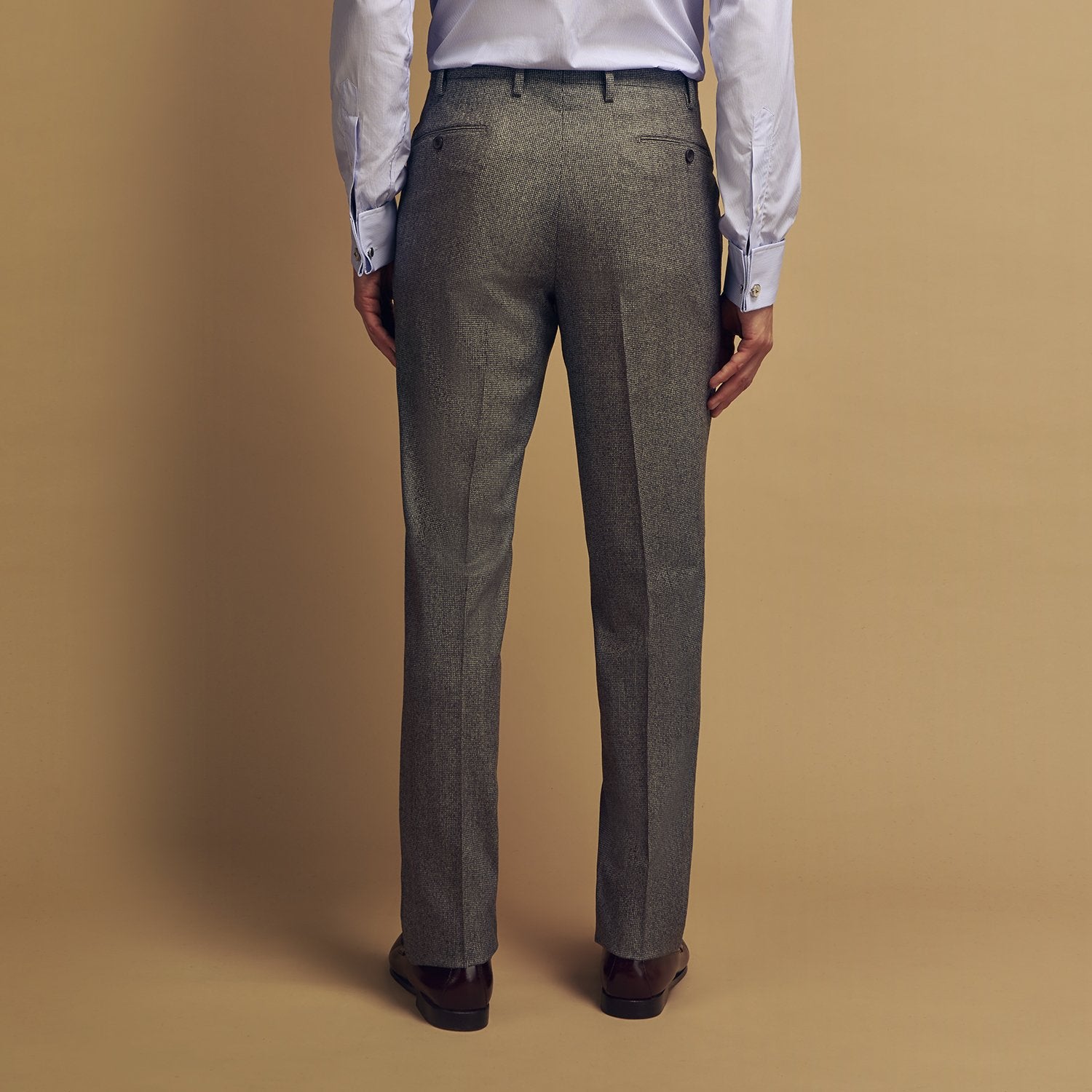 View 6 of product A person wears Turnbull & Asser Grey Puppytooth Wool Manson Trousers, a white dress shirt with rolled-up sleeves, and black shoes, standing against a plain beige background.