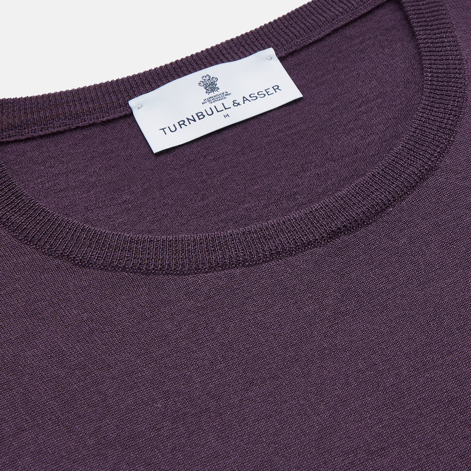 View 2 of product The Turnbull & Asser Plum Kingston Merino Crew Neck Jumper is a lightweight, long-sleeve sweater with ribbed cuffs and hem, shown flat on a white background. Its solid plum color and classic design offer timeless style.