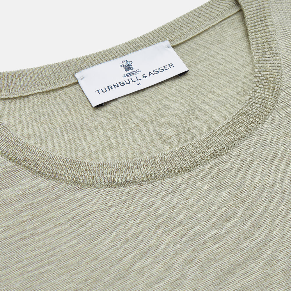 The Light Green Kingston Merino Crew Neck Jumper by Turnbull & Asser is laid flat, displaying its classic design with ribbed cuffs, hem, and neckline.