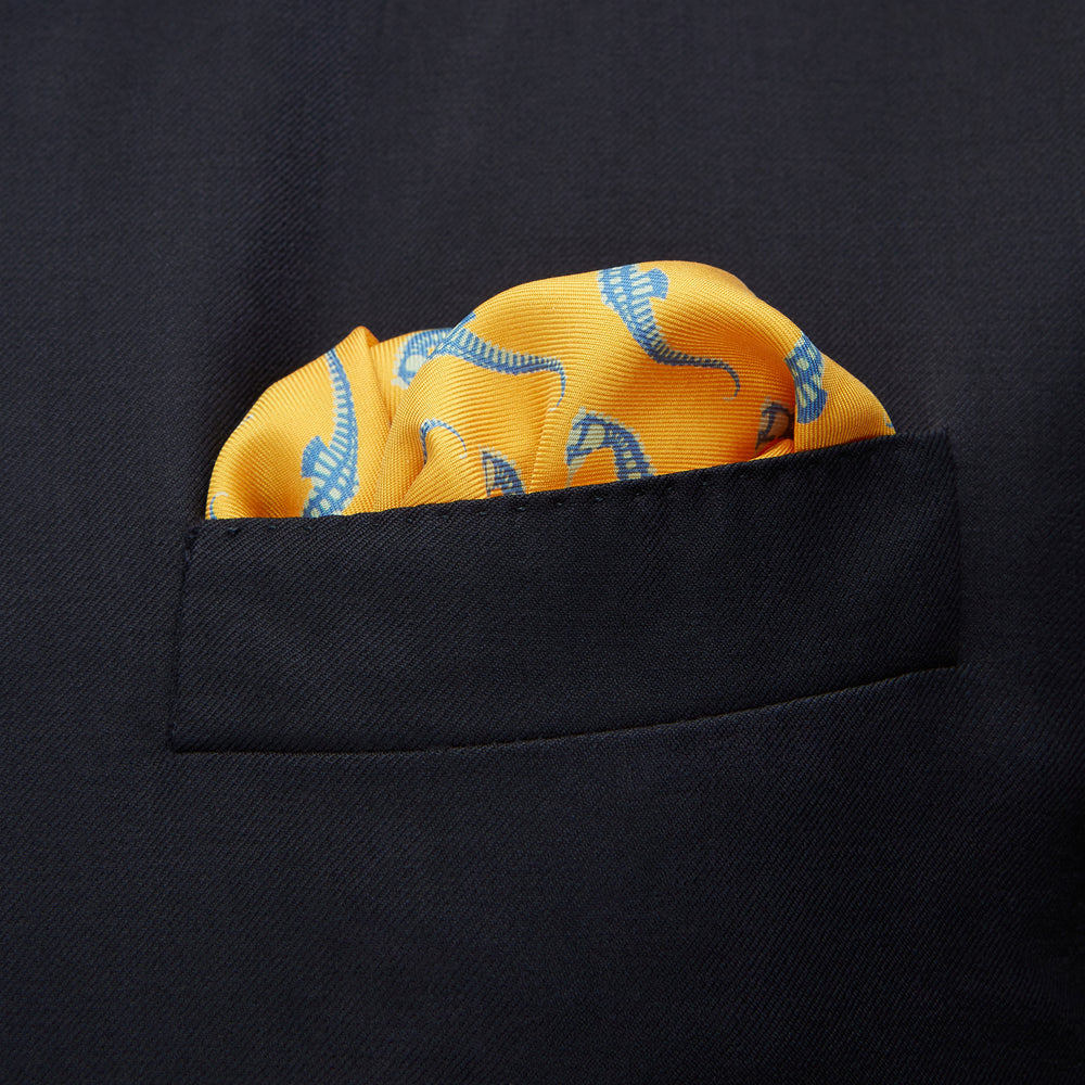 The Turnbull & Asser Yellow & Blue Seahorse Silk Pocket Square features a repeating seahorse pattern in diagonal rows and is handprinted in England, with branding in two corners.