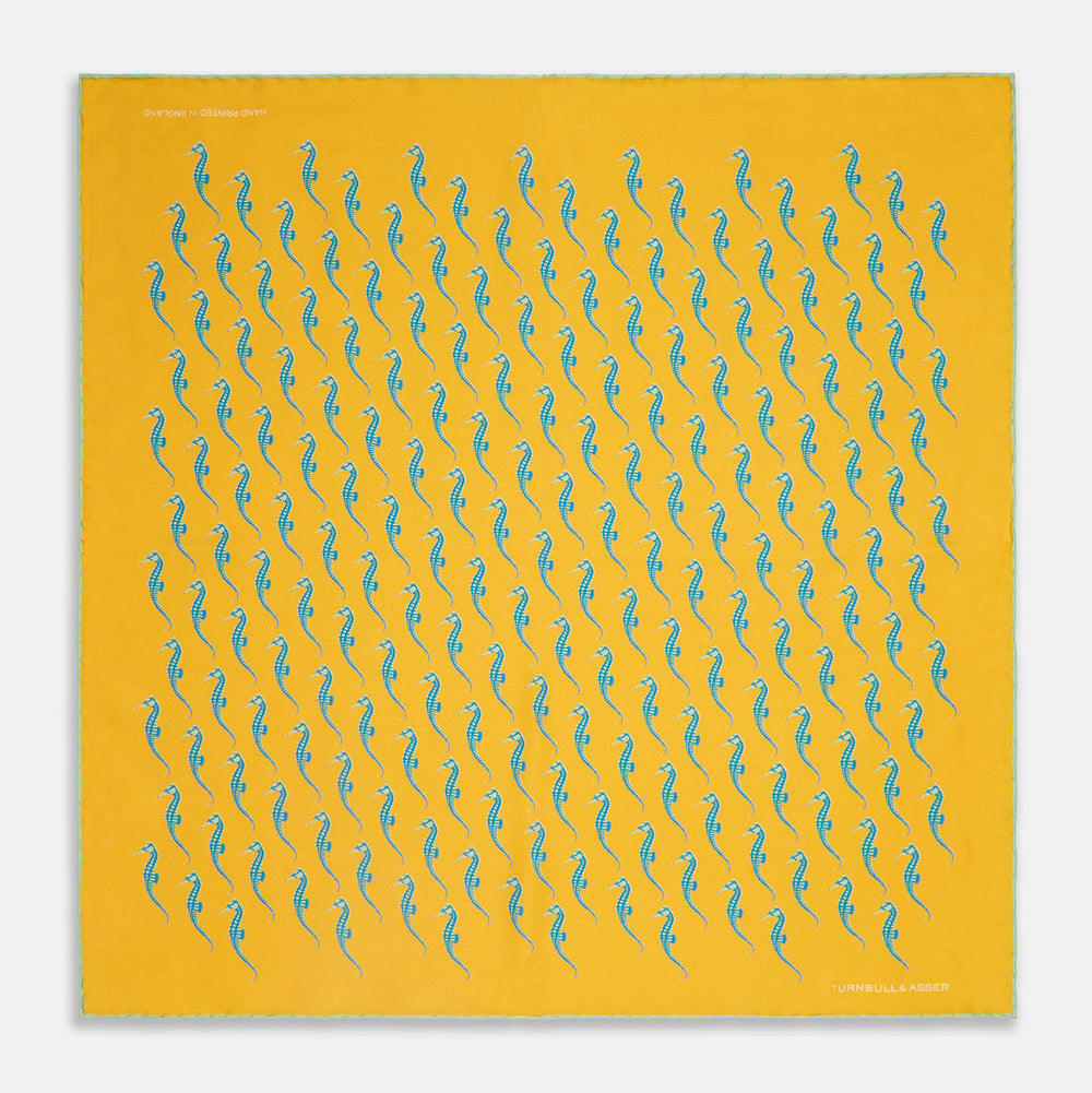 The Turnbull & Asser Yellow & Blue Seahorse Silk Pocket Square features a repeating seahorse pattern in diagonal rows and is handprinted in England, with branding in two corners.