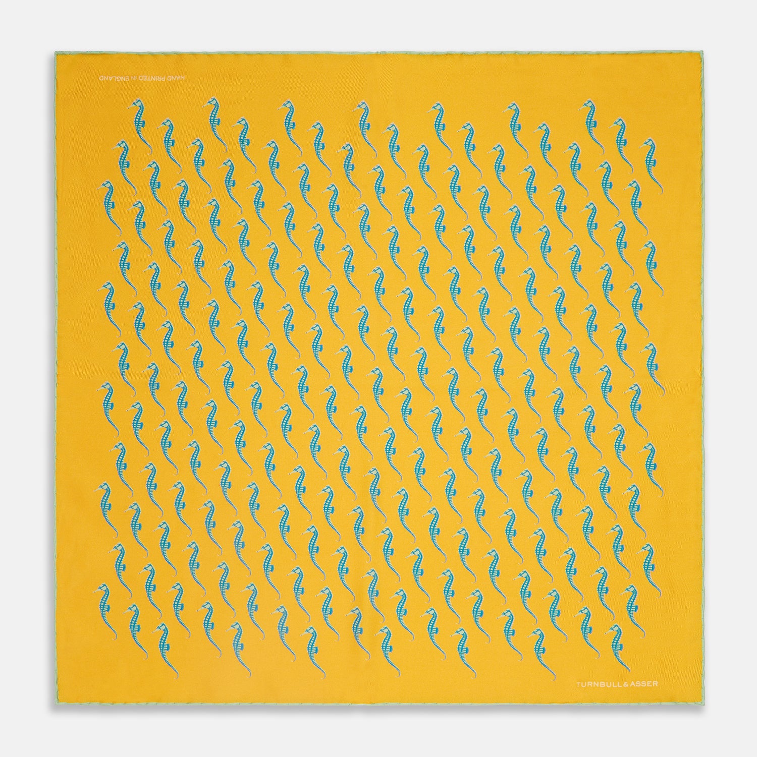 View 1 of product The Turnbull & Asser Yellow & Blue Seahorse Silk Pocket Square features a repeating seahorse pattern in diagonal rows and is handprinted in England, with branding in two corners.
