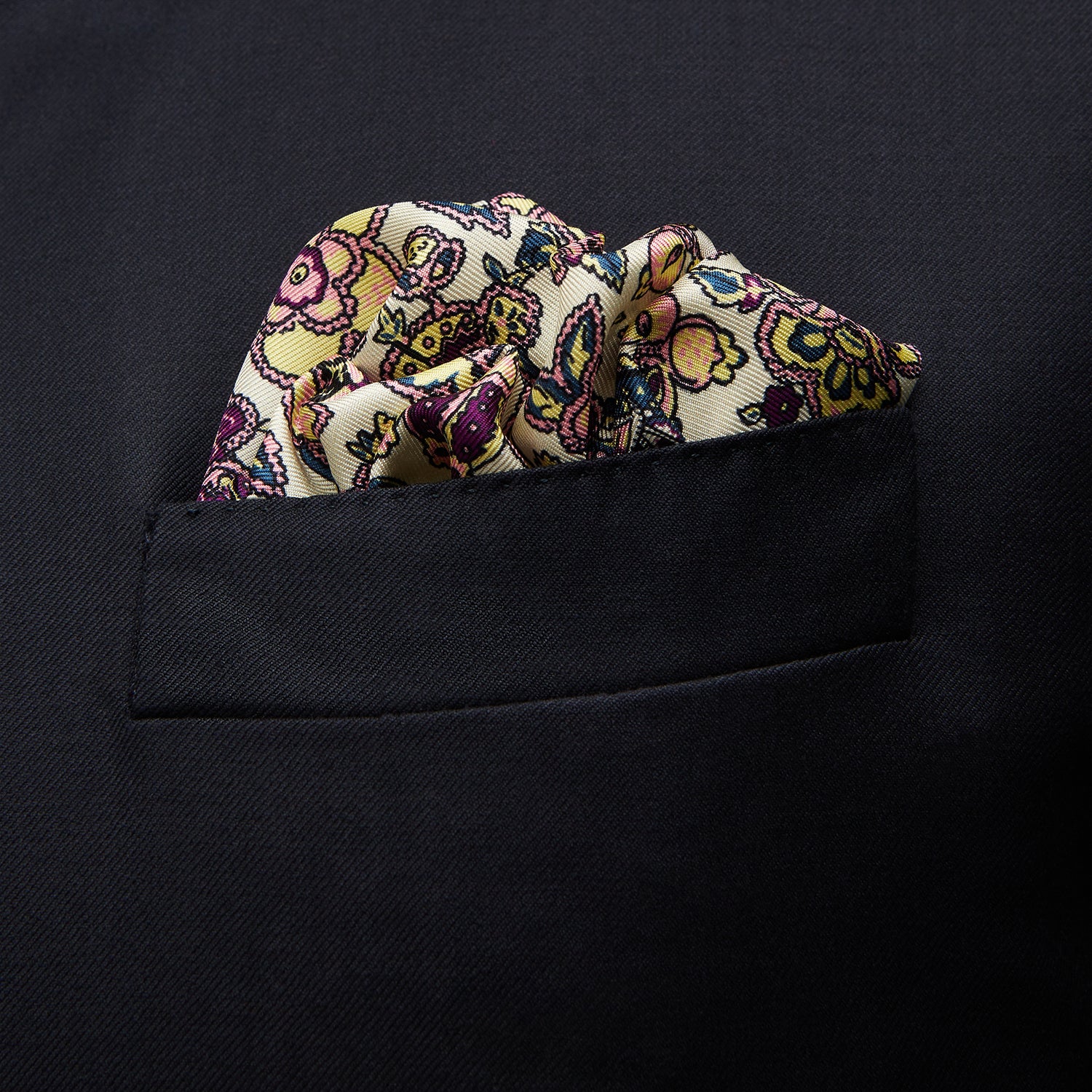 View 3 of product The White Floral Silk Pocket Square by Turnbull & Asser is crafted in England from silk, featuring a floral and paisley design in pink, purple, and gold with a navy border and the "TURNBULL & ASSER" logo in the corner.