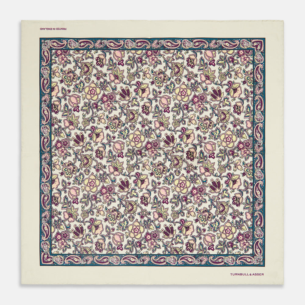 The White Floral Silk Pocket Square by Turnbull & Asser is crafted in England from silk, featuring a floral and paisley design in pink, purple, and gold with a navy border and the "TURNBULL & ASSER" logo in the corner.
