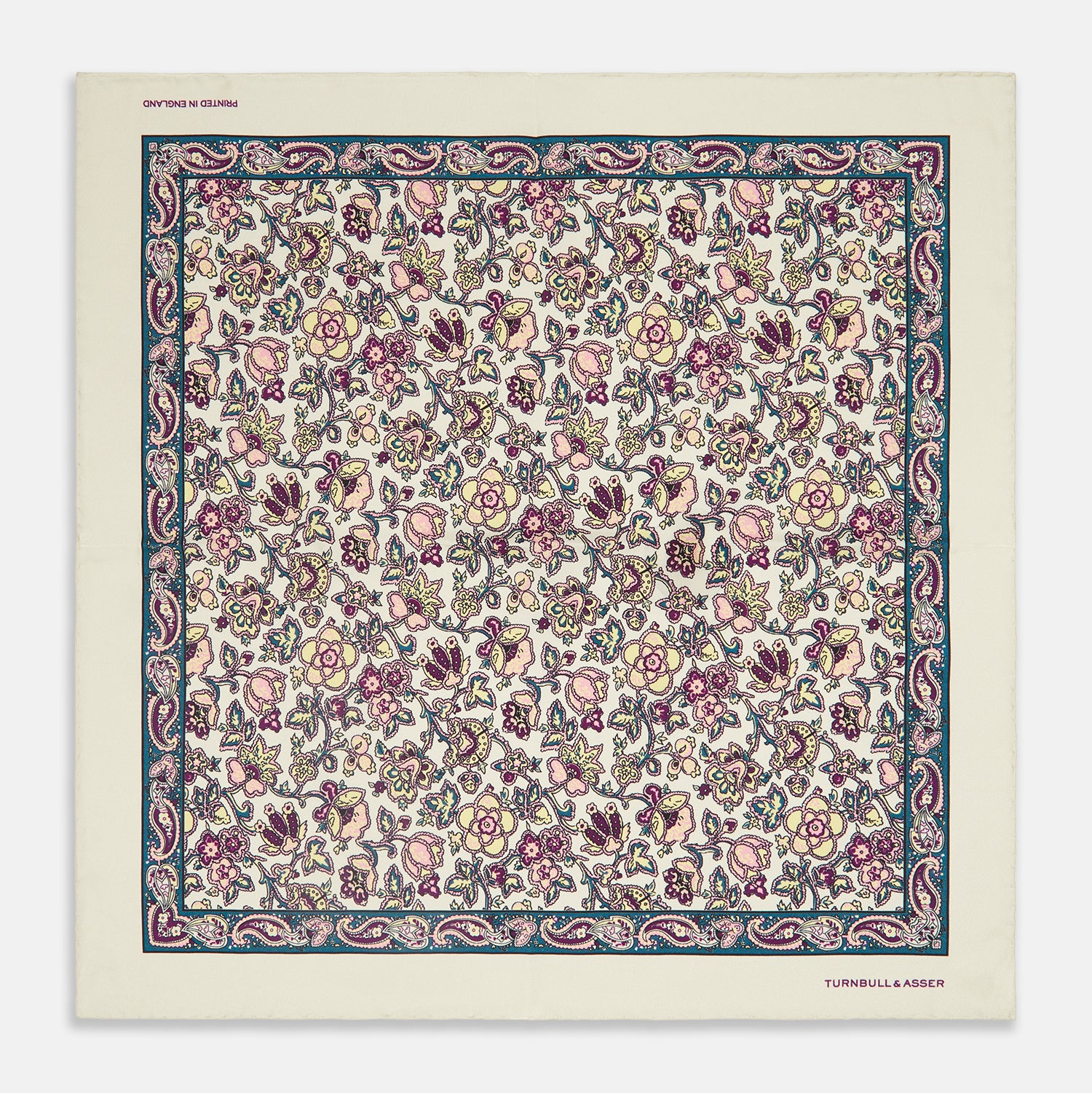 View 1 of product The White Floral Silk Pocket Square by Turnbull & Asser is crafted in England from silk, featuring a floral and paisley design in pink, purple, and gold with a navy border and the "TURNBULL & ASSER" logo in the corner.