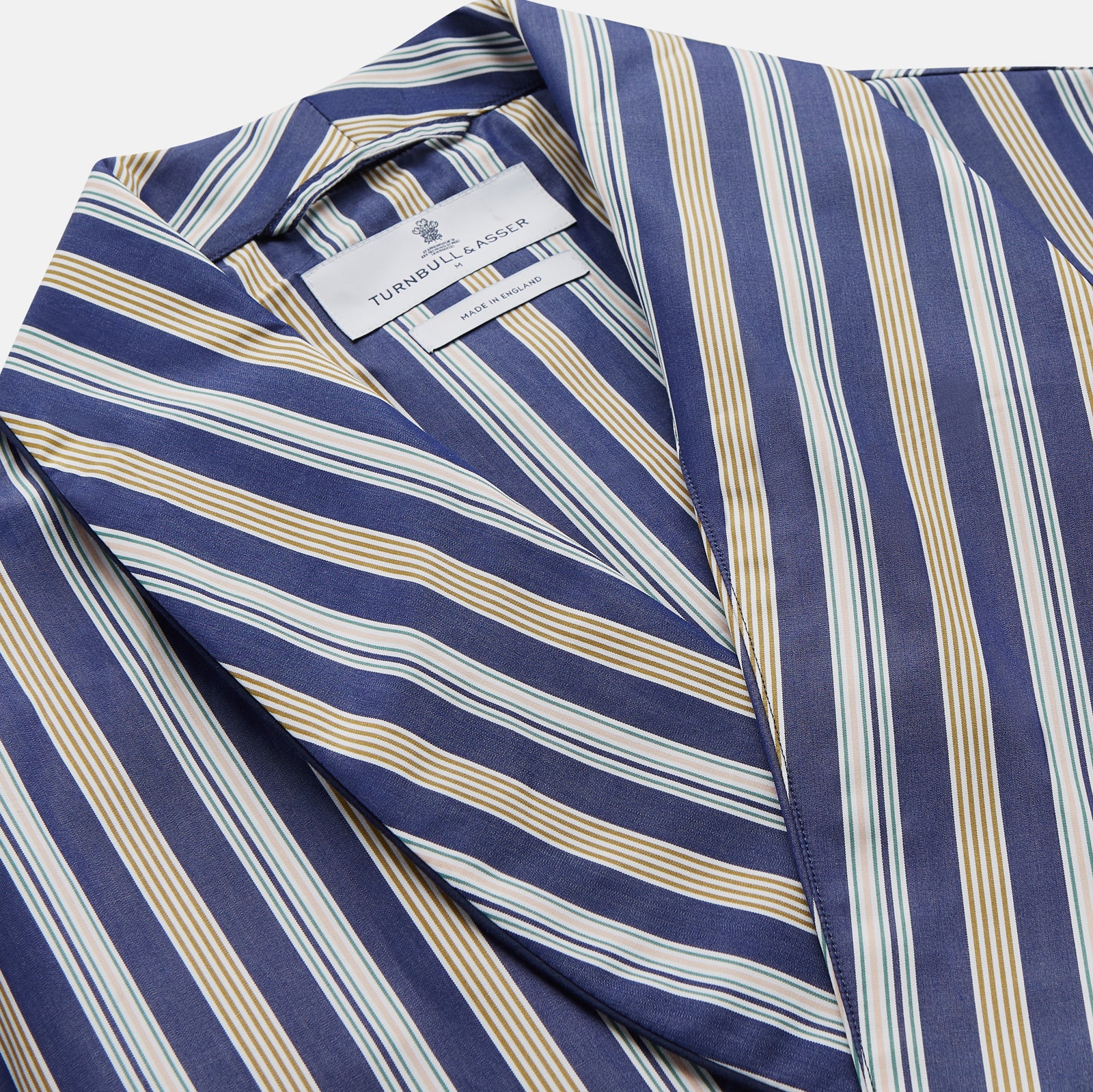 View 3 of product The Turnbull & Asser Blue Multi Stripe Cotton Gown features blue and white vertical stripes, long sleeves, a shawl collar, front pockets, and a matching waist tie, shown on a plain white background.