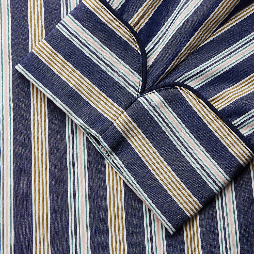 The Turnbull & Asser Blue Multi Stripe Cotton Gown features blue and white vertical stripes, long sleeves, a shawl collar, front pockets, and a matching waist tie, shown on a plain white background.