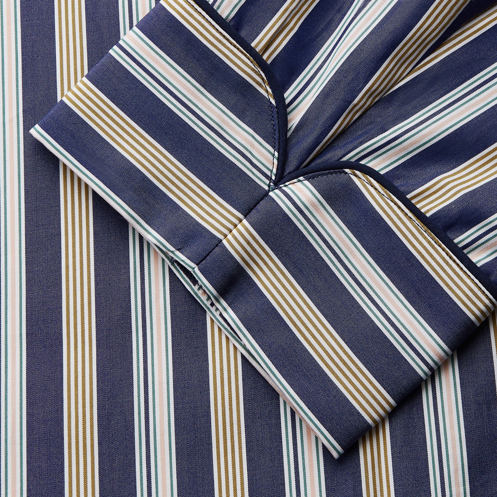 View 4 of product The Turnbull & Asser Blue Multi Stripe Cotton Gown features blue and white vertical stripes, long sleeves, a shawl collar, front pockets, and a matching waist tie, shown on a plain white background.