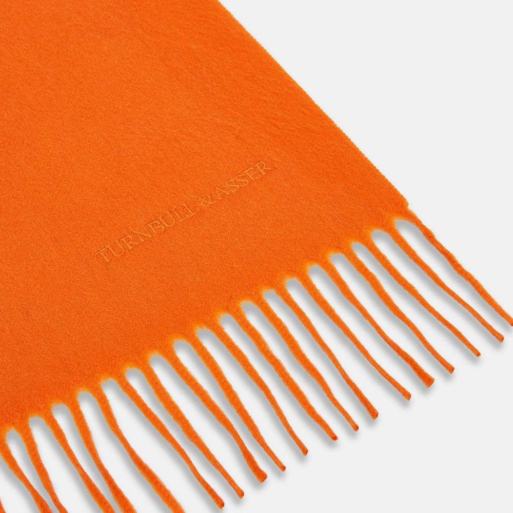 The Turnbull & Asser Orange Purled Fringe Cashmere Scarf is shown neatly arranged on a white background, featuring soft, thick cashmere with fringe at both ends and a subtle embroidered logo near one edge.