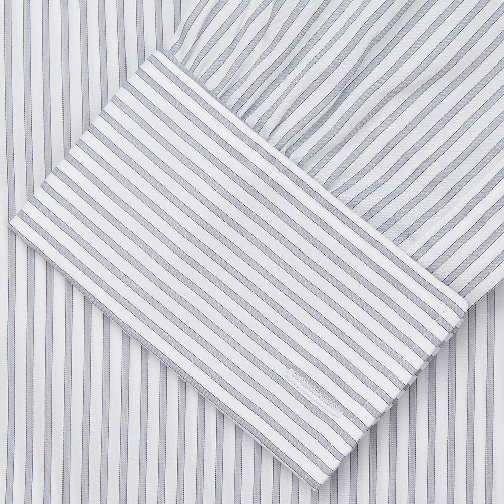 A man wearing the Turnbull & Asser Grey Multi Stripe Regular Fit Twill Shirt with T&A Collar and Double Cuffs stands against a beige background, one hand in his pocket, looking at the camera.