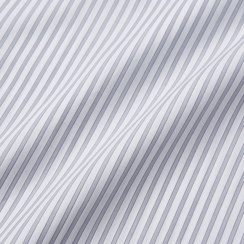 A man wearing the Turnbull & Asser Grey Multi Stripe Regular Fit Twill Shirt with T&A Collar and Double Cuffs stands against a beige background, one hand in his pocket, looking at the camera.