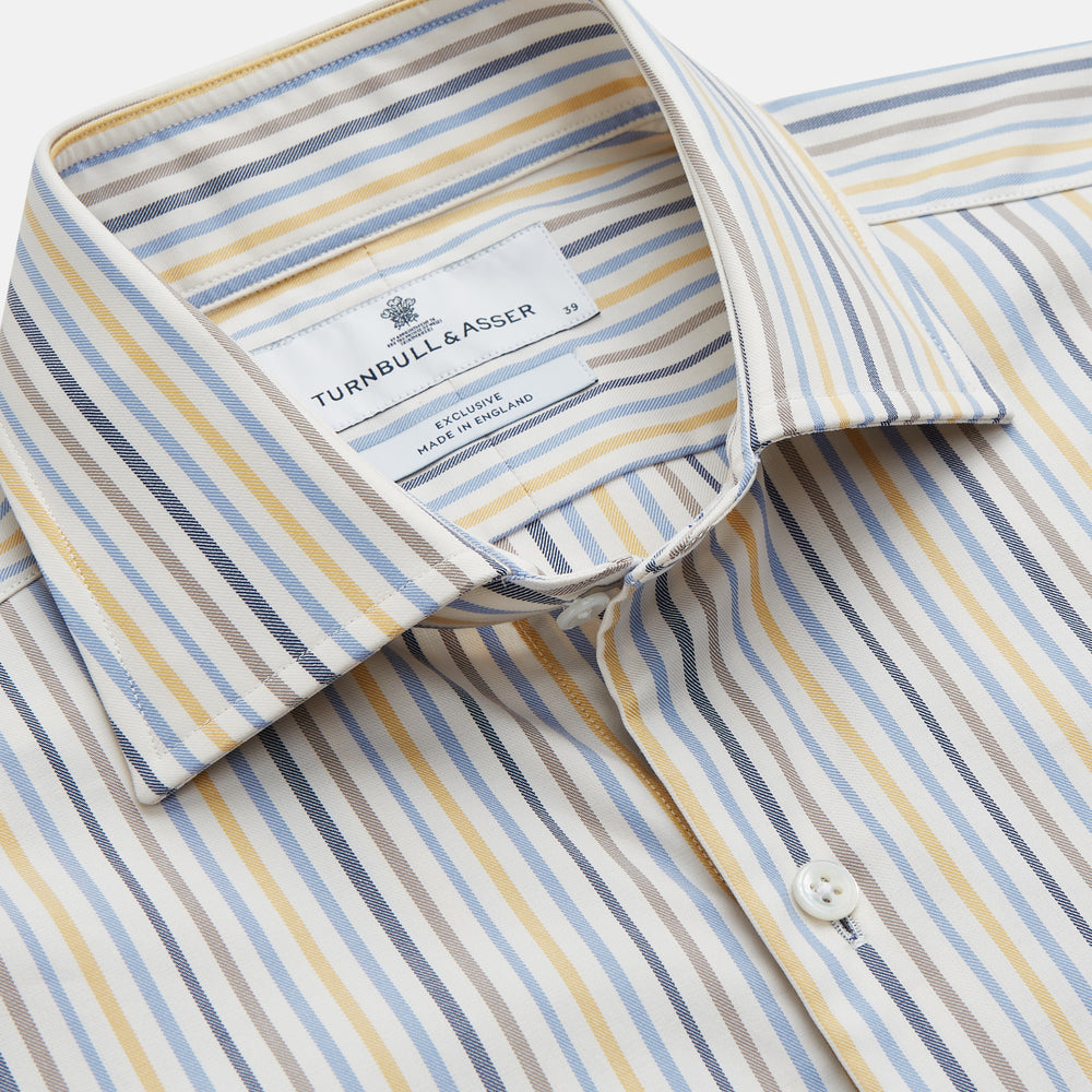 Turnbull & Asser’s Yellow Multi Stripe Tailored Fit Shirt features a Kent collar, blue, yellow, and white stripes on a light background, 2-button cuffs, and a curved hem for a refined look.