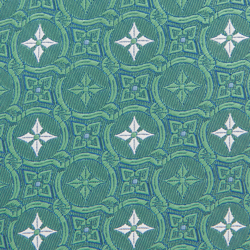 The Turnbull & Asser Green Multi Neat Silk Tie, handmade and featuring a white and light blue geometric pattern, is shown rolled up on a plain white background.