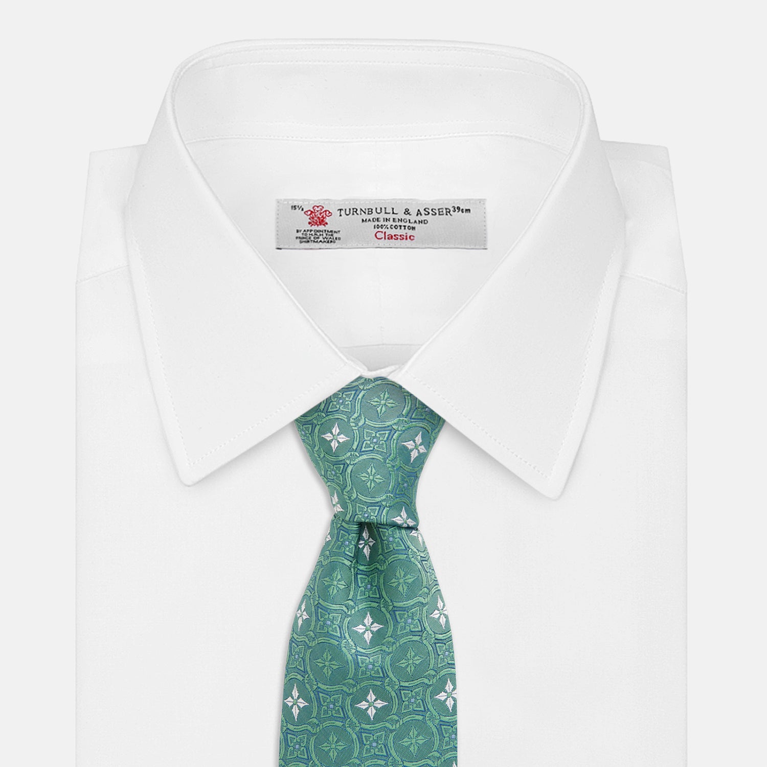 View 2 of product The Turnbull & Asser Green Multi Neat Silk Tie, handmade and featuring a white and light blue geometric pattern, is shown rolled up on a plain white background.