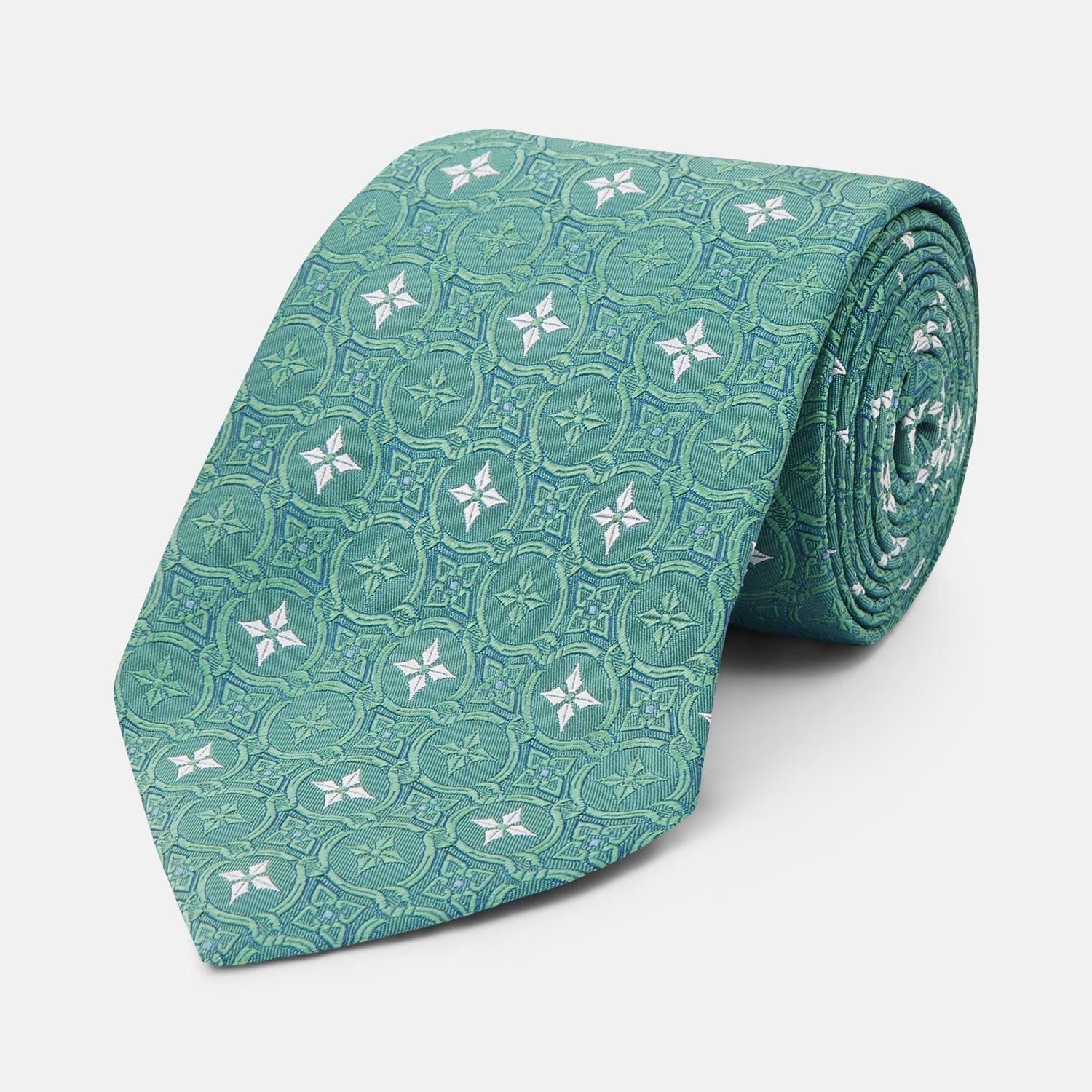 View 1 of product The Turnbull & Asser Green Multi Neat Silk Tie, handmade and featuring a white and light blue geometric pattern, is shown rolled up on a plain white background.