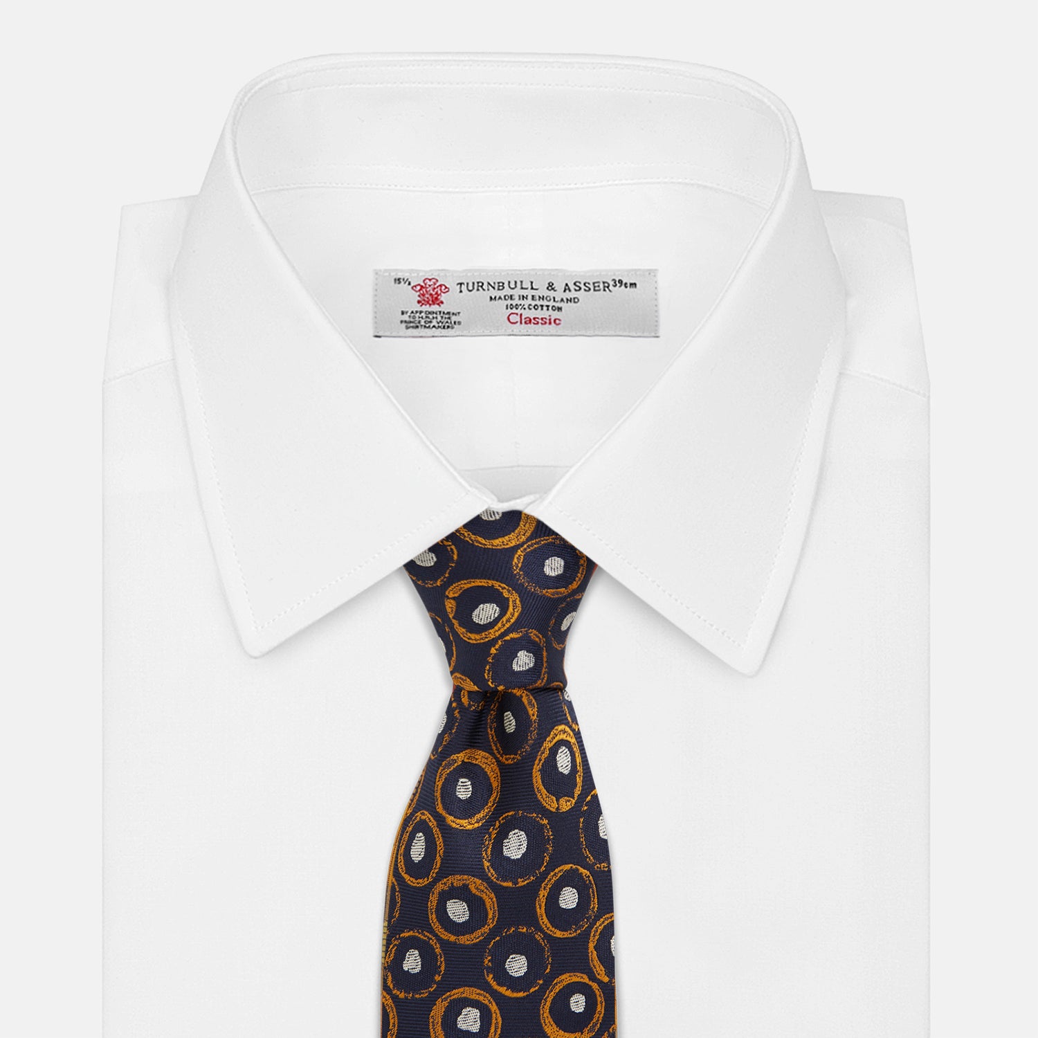 View 2 of product The Turnbull & Asser Orange Multi Circle Printed Silk Tie features navy blue silk with orange circles and white ovals, perfect for elevating any formal outfit. Shown on a plain white background.