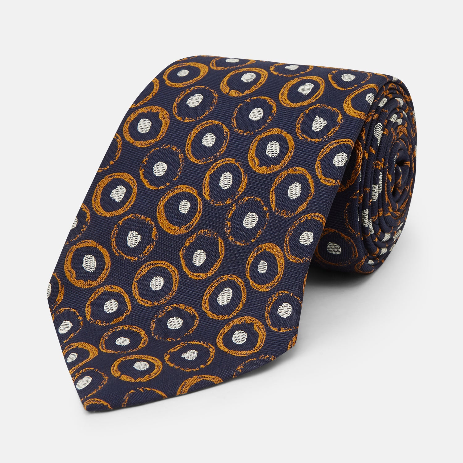 View 1 of product The Turnbull & Asser Orange Multi Circle Printed Silk Tie features navy blue silk with orange circles and white ovals, perfect for elevating any formal outfit. Shown on a plain white background.