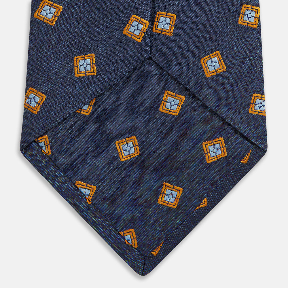 The Turnbull & Asser Orange Multi Geo Silk Tie, featuring a vibrant geometric pattern, is showcased rolled up on a plain white background—an elegant piece from our autumn-winter collection.