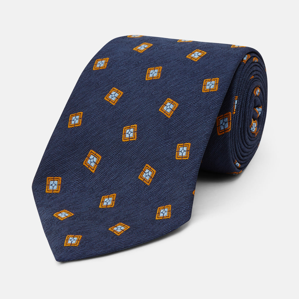 The Turnbull & Asser Orange Multi Geo Silk Tie, featuring a vibrant geometric pattern, is showcased rolled up on a plain white background—an elegant piece from our autumn-winter collection.