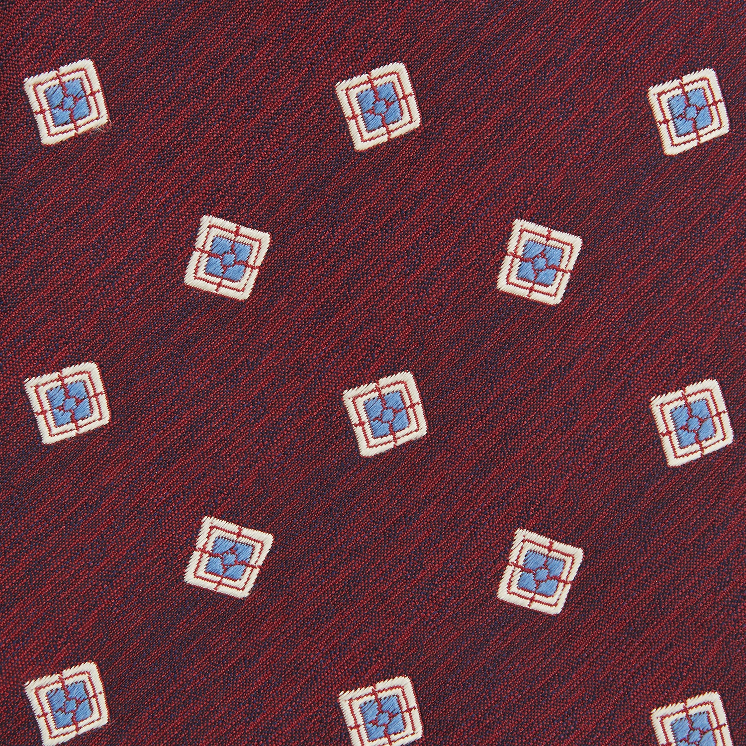View 3 of product The Turnbull & Asser Burgundy Multi Geo Silk Tie features burgundy silk with blue, white, and yellow geometric designs—ideal for bold statement shirts. Shown rolled against a plain white background.