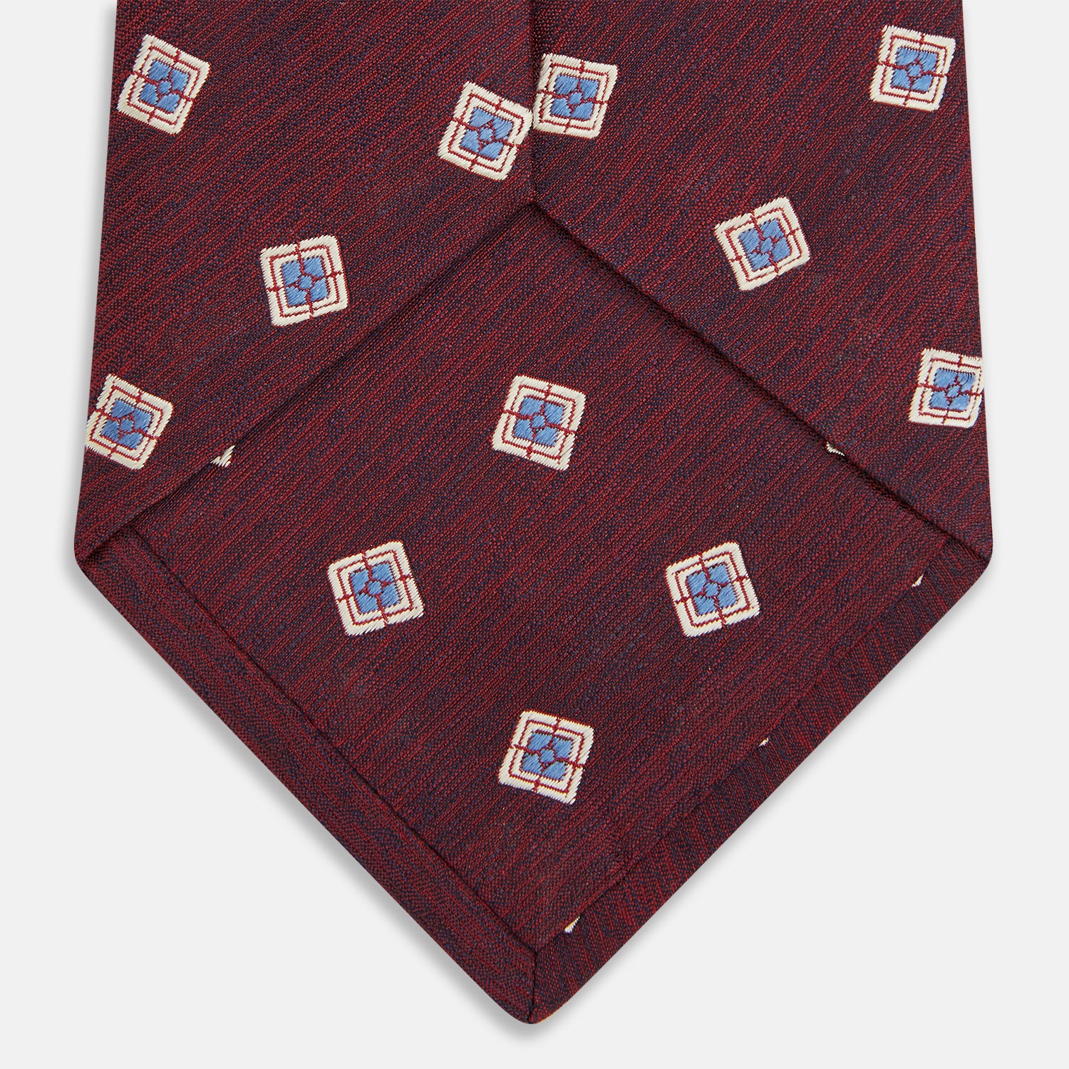 View 4 of product The Turnbull & Asser Burgundy Multi Geo Silk Tie features burgundy silk with blue, white, and yellow geometric designs—ideal for bold statement shirts. Shown rolled against a plain white background.