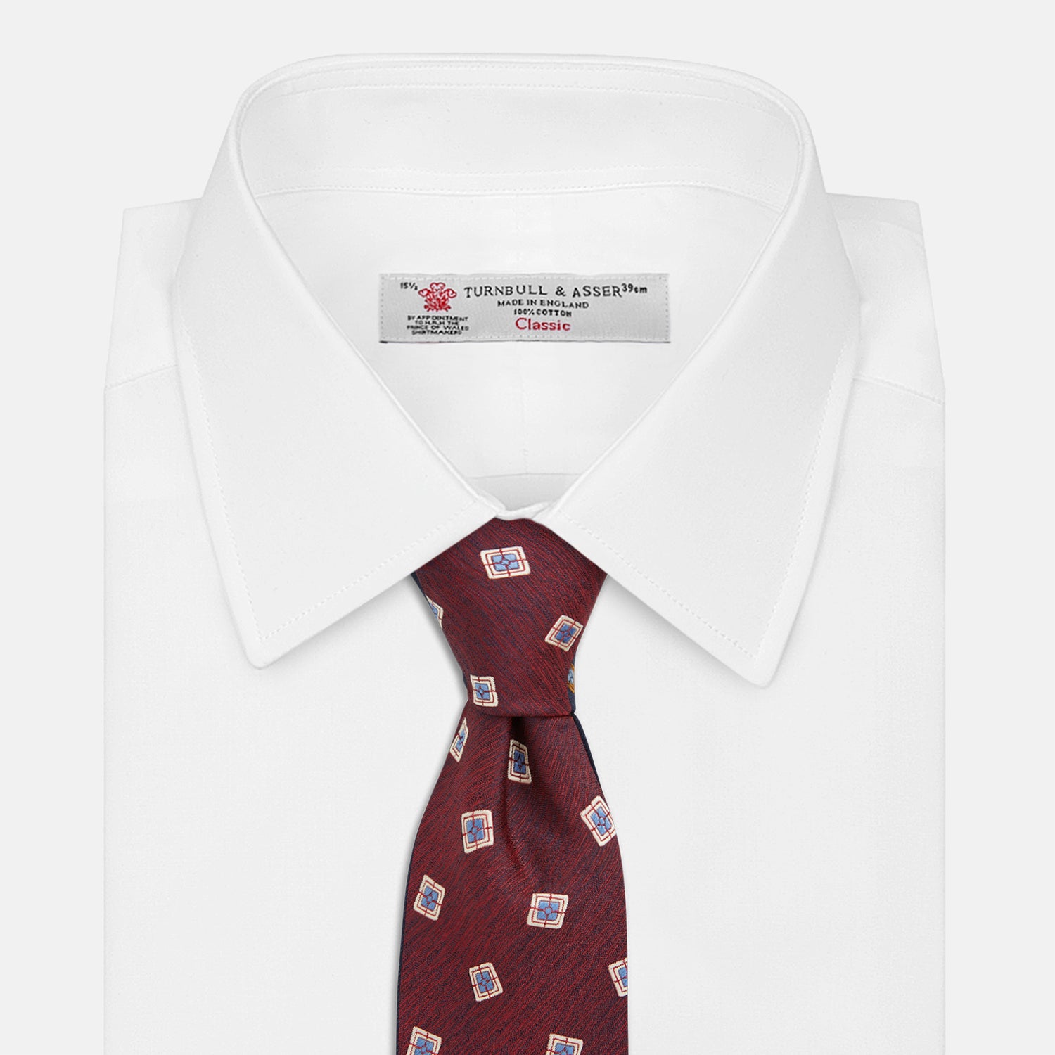 View 2 of product The Turnbull & Asser Burgundy Multi Geo Silk Tie features burgundy silk with blue, white, and yellow geometric designs—ideal for bold statement shirts. Shown rolled against a plain white background.