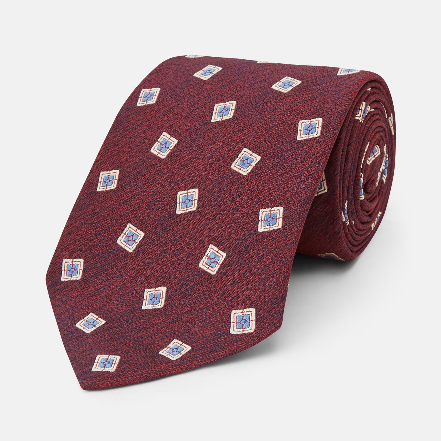 View 1 of product The Turnbull & Asser Burgundy Multi Geo Silk Tie features burgundy silk with blue, white, and yellow geometric designs—ideal for bold statement shirts. Shown rolled against a plain white background.
