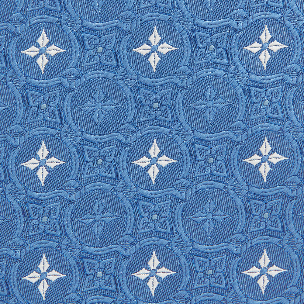The Blue Multi Neat Silk Tie by Turnbull & Asser features a geometric pattern of white four-pointed shapes and circles, crafted in blue silk from the autumn-winter collection. Displayed rolled on a plain light background.