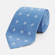 The Blue Multi Neat Silk Tie by Turnbull & Asser features a geometric pattern of white four-pointed shapes and circles, crafted in blue silk from the autumn-winter collection. Displayed rolled on a plain light background.