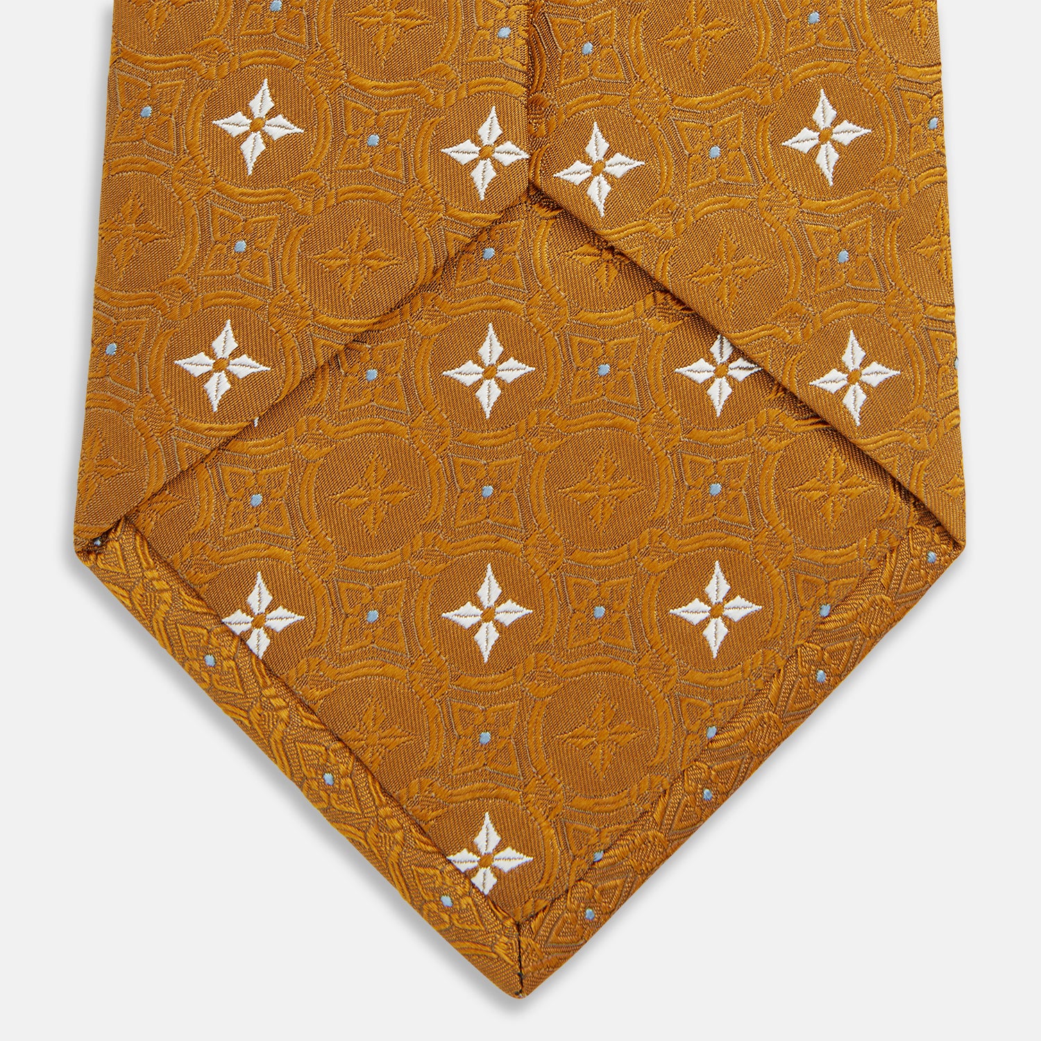 View 4 of product The Orange Multi Neat Silk Tie by Turnbull & Asser, from the autumn-winter collection, features a golden yellow geometric pattern on textured silk. Shown rolled on a white background, it pairs perfectly with bold signature shirts.
