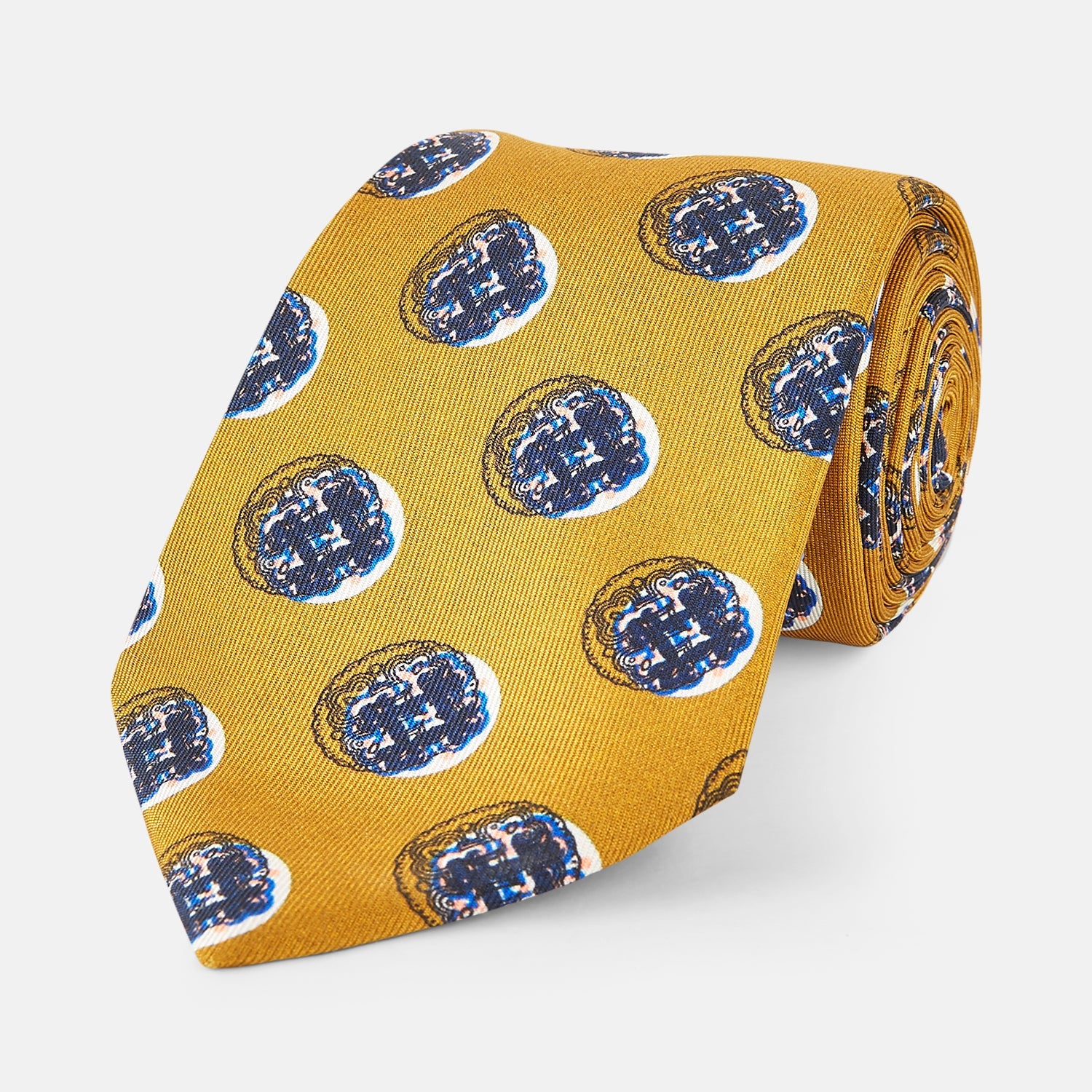 View 1 of product A rolled-up Turnbull & Asser Gold Shadow Spot Printed Silk Tie, featuring blue and white circular patterns on fine Adamley Macclesfield silk, displayed against a white background.