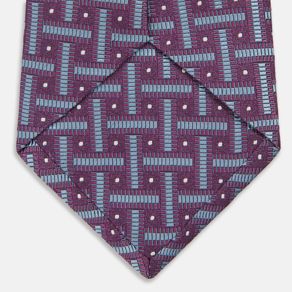 The Turnbull & Asser Purple & Navy Cross Silk Tie features a geometric pattern of intersecting blue lines and white dots—an ideal accessory to elevate formal outfits or complement signature shirts.