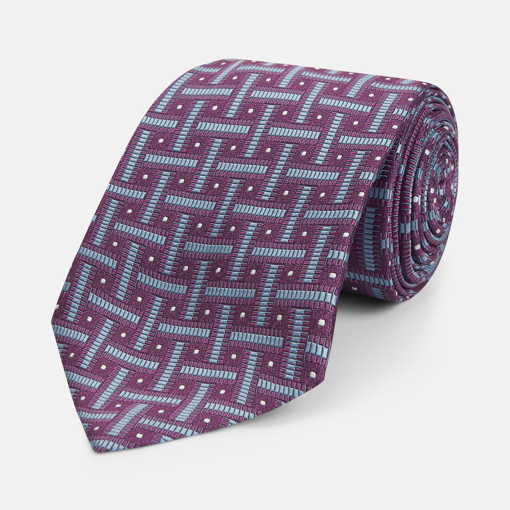 The Turnbull & Asser Purple & Navy Cross Silk Tie features a geometric pattern of intersecting blue lines and white dots—an ideal accessory to elevate formal outfits or complement signature shirts.