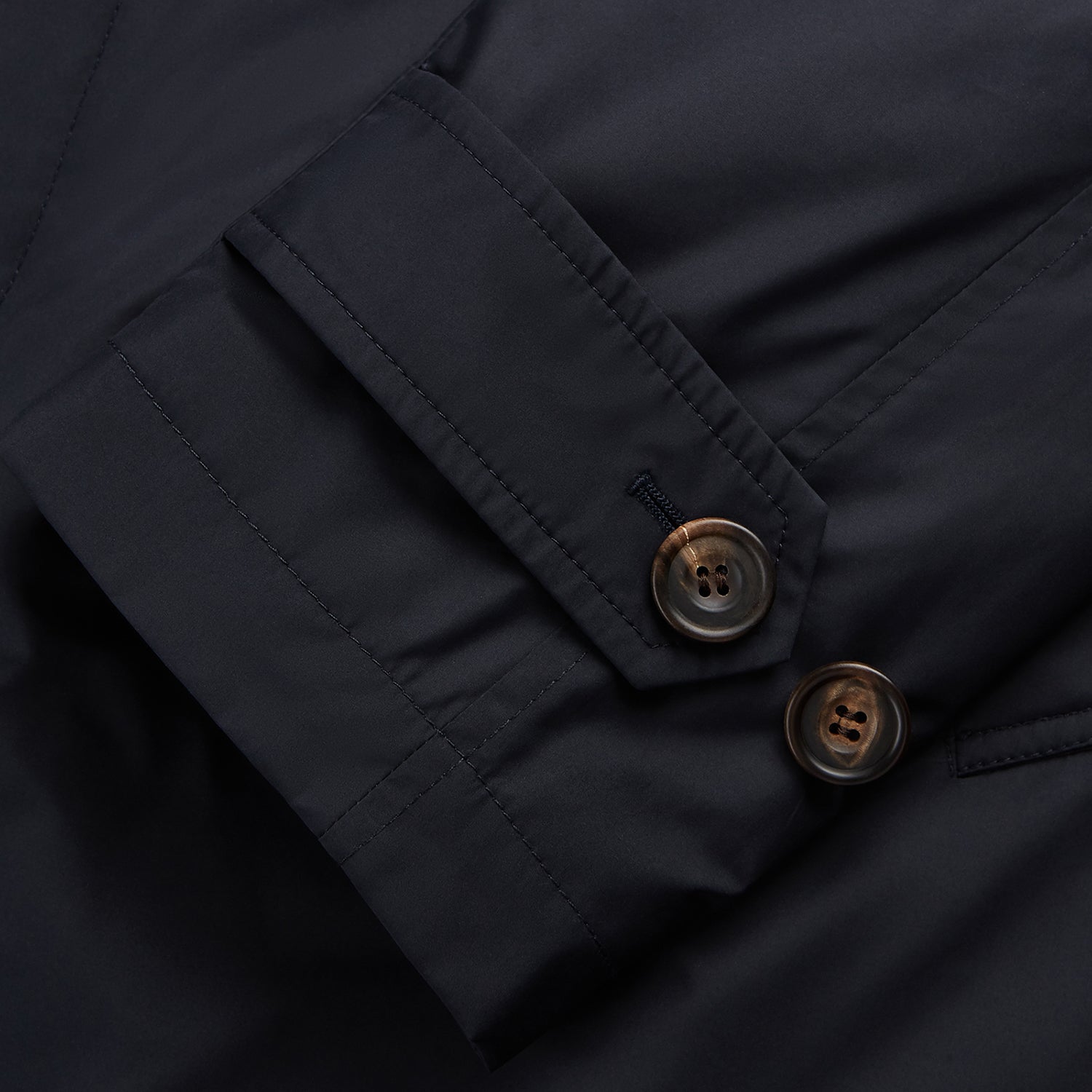 View 4 of product A man with brown hair stands outdoors, hands in his pockets, wearing a Turnbull & Asser Navy Sealup Quilted Liner Quintern Car Coat over a mustard cardigan. A glass barrier and blurred background are behind him.