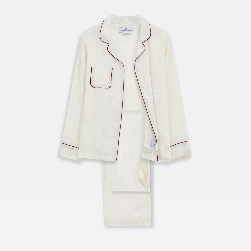 The Cream Floral Pattern Silk Harriet Women's Pyjama Set by Turnbull & Asser features long sleeves, pants, dark piping, a chest pocket, and luxurious silk fabric with a cream floral design, shown on a plain white background.