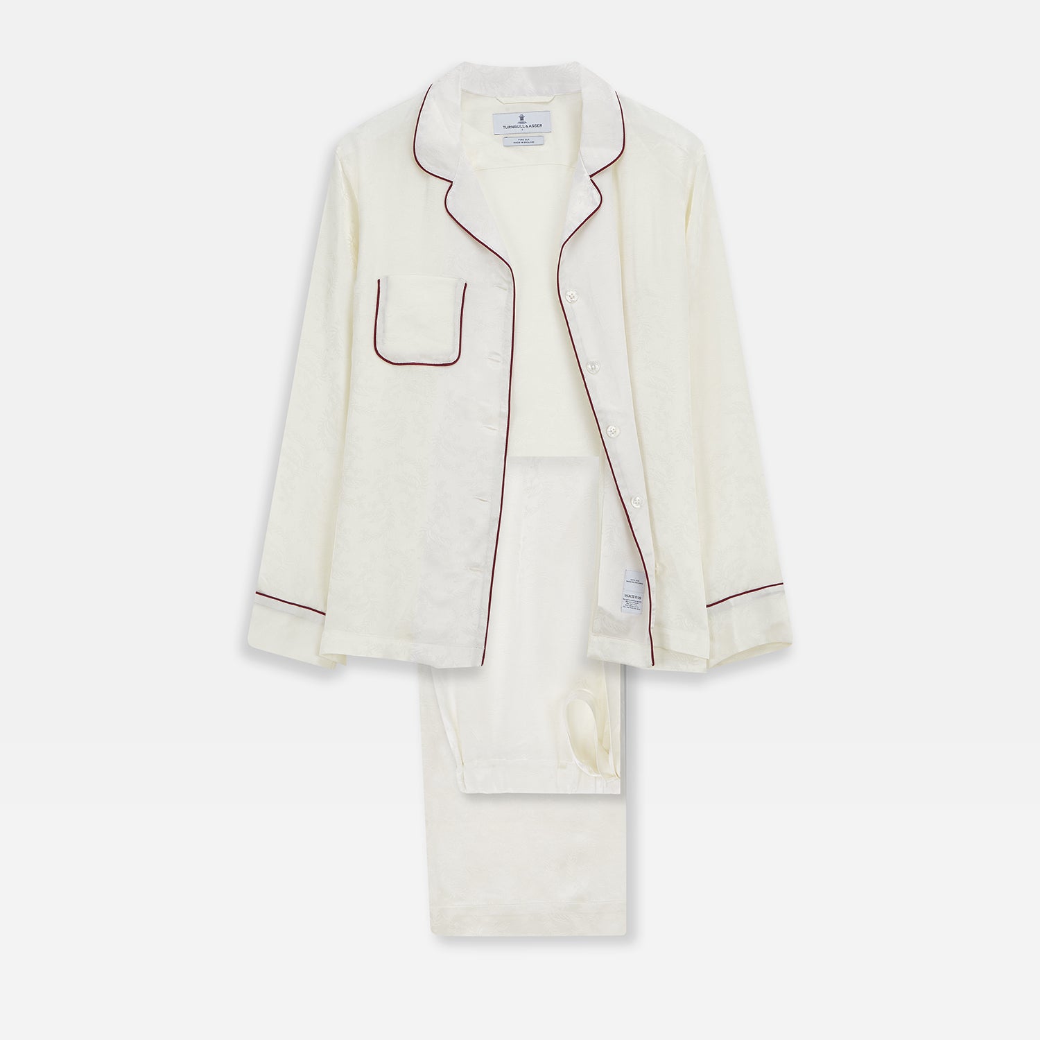 View 1 of product The Cream Floral Pattern Silk Harriet Women's Pyjama Set by Turnbull & Asser features long sleeves, pants, dark piping, a chest pocket, and luxurious silk fabric with a cream floral design, shown on a plain white background.