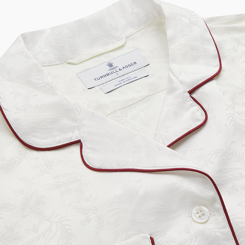 The Cream Floral Pattern Silk Harriet Women's Pyjama Set by Turnbull & Asser features long sleeves, pants, dark piping, a chest pocket, and luxurious silk fabric with a cream floral design, shown on a plain white background.